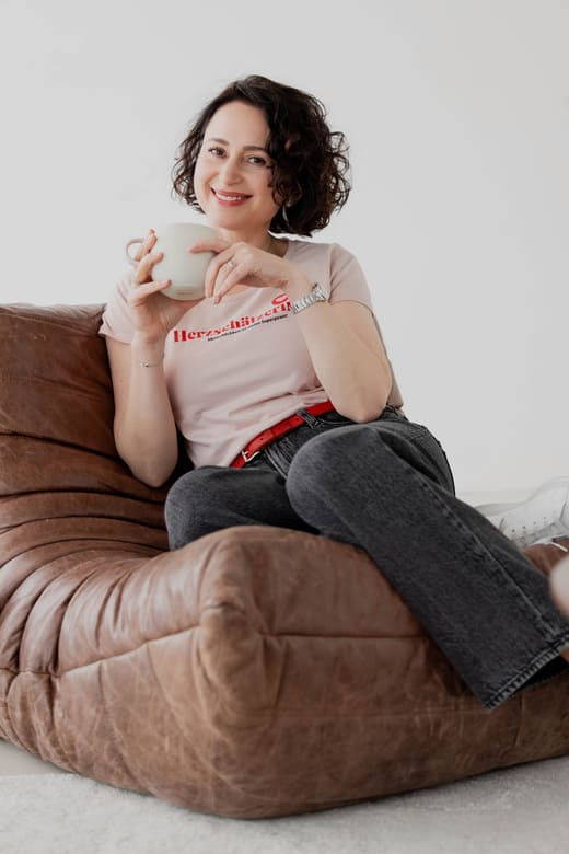 Herzschätzerin, Claudia di Chio, sitzend auf einem braunen Sessel, eine Tasse in der Hand haltend