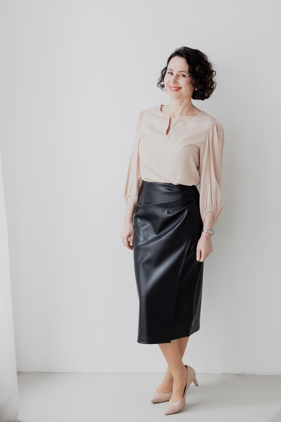 herzschaetzerin-claudia-di-chio-resilianz-menschlichkeit Herzschätzerin, Claudia di Chio stehend mit überkreuzten Beinen an weißer Wand.